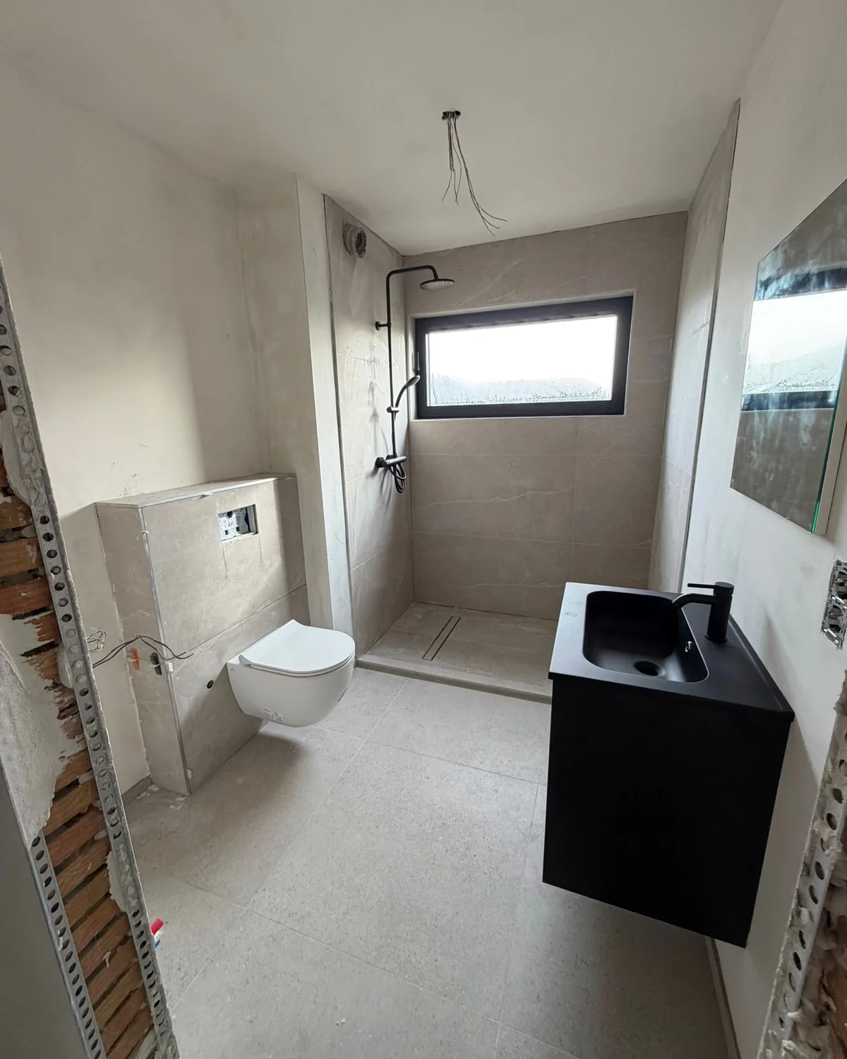 Dezelfde badkamer afgewerkt met een inloopdouche met zwarte regendouche, een hangtoilet, een zwart badmeubel en grote wandtegels