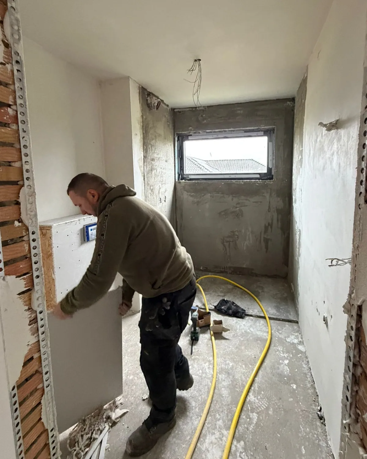 Badkamer in Herentals tijdens de werken: een vakman werkt een inbouwframe van het toilet af, de muren zijn bepleisterd en de vloer is nog ruw