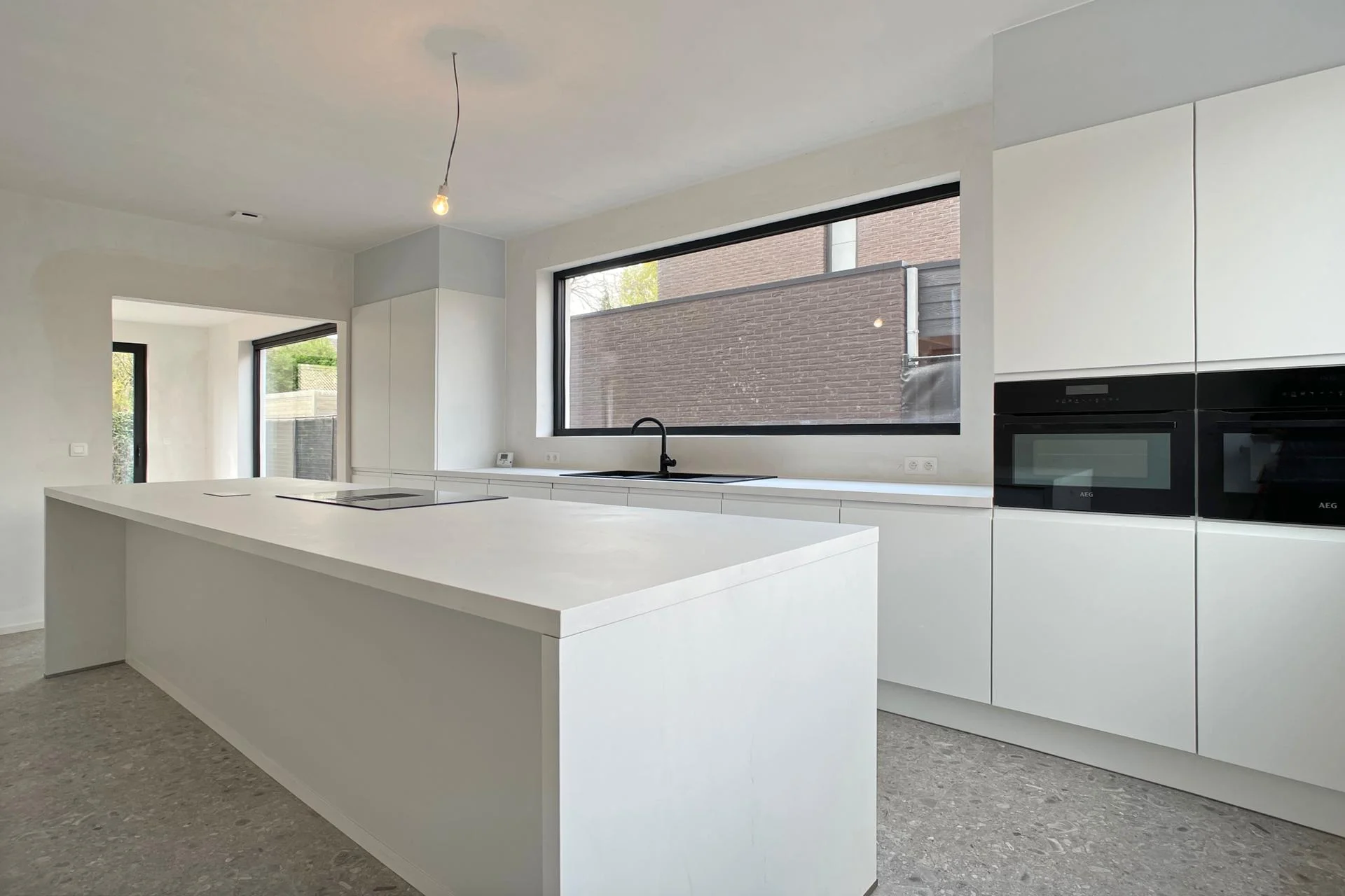 Renovated white kitchen with an island, built-in appliances and a concrete floor