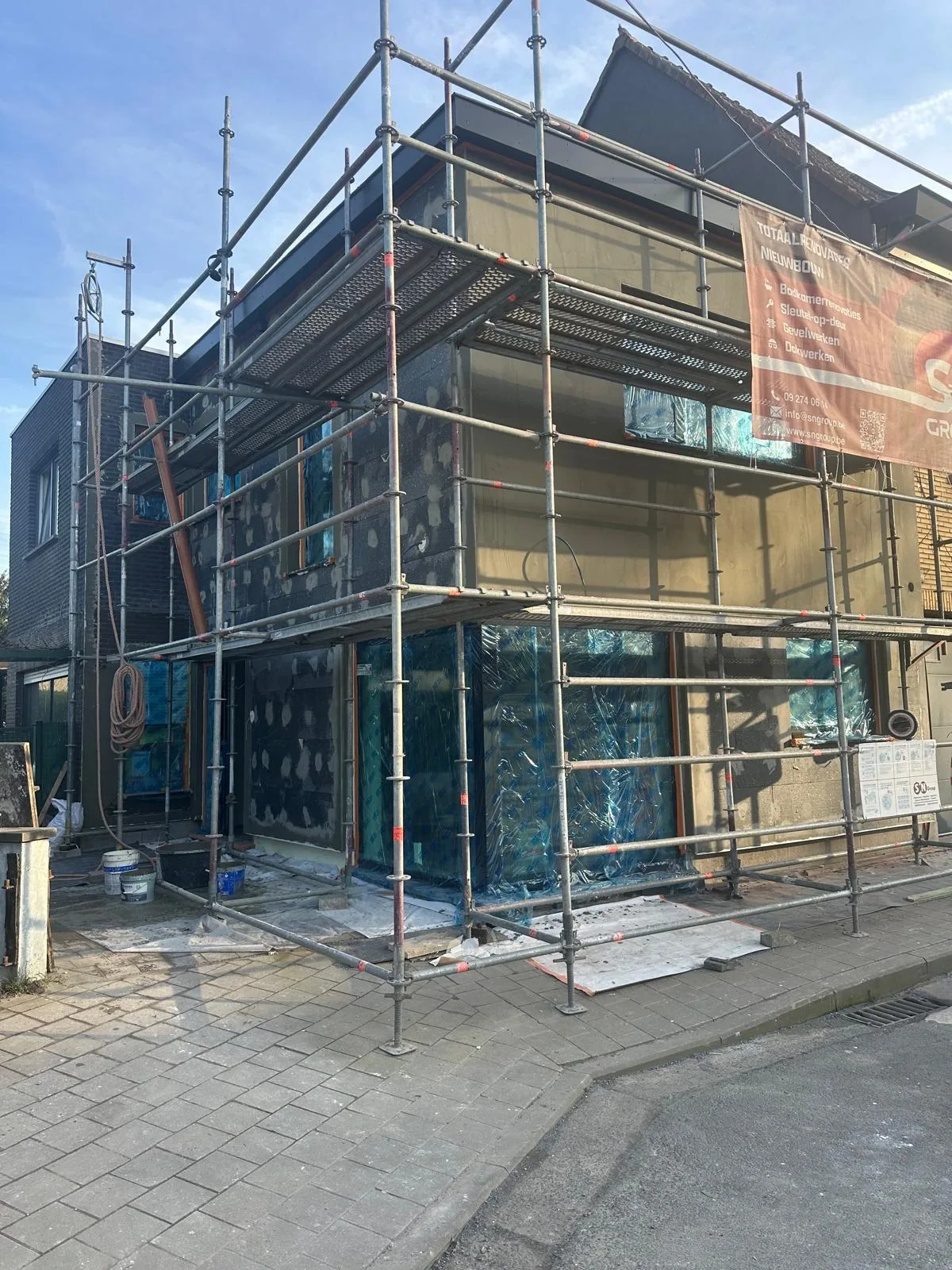 Gevelrenovatie in Gent onder een stelling, met isolatieplaten, afgeplakte ramen en een werfbord van SN Group