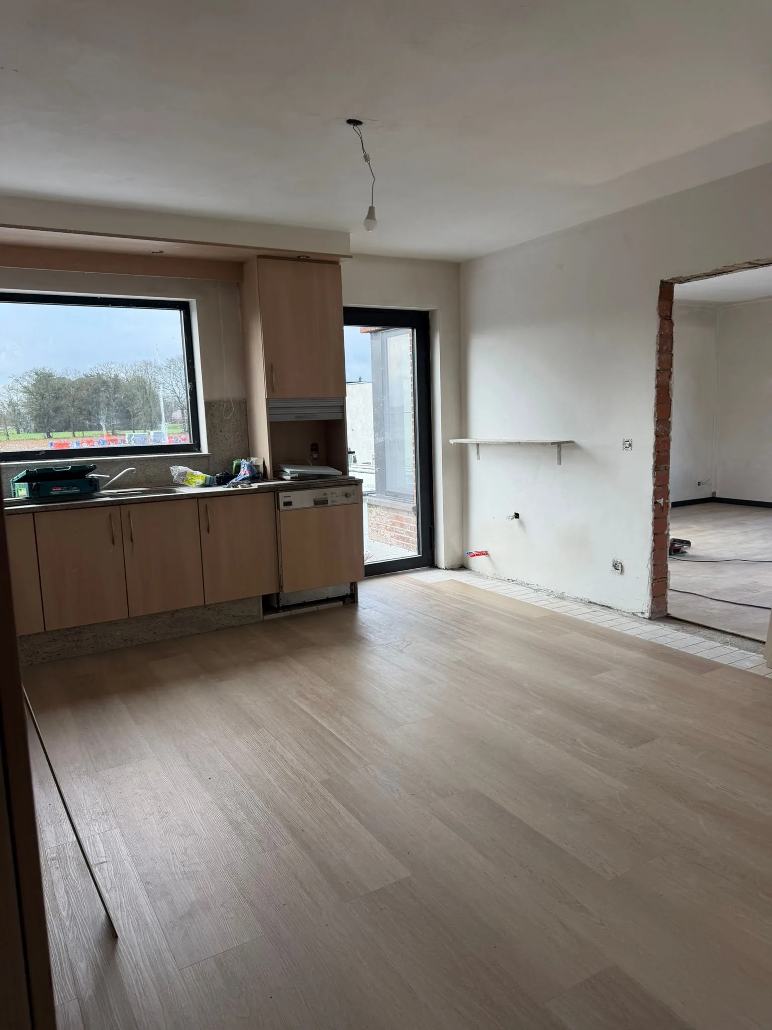 Leefruimte met keukenkasten in houtdecor, een nieuwe laminaatvloer en een glazen deur naar buiten