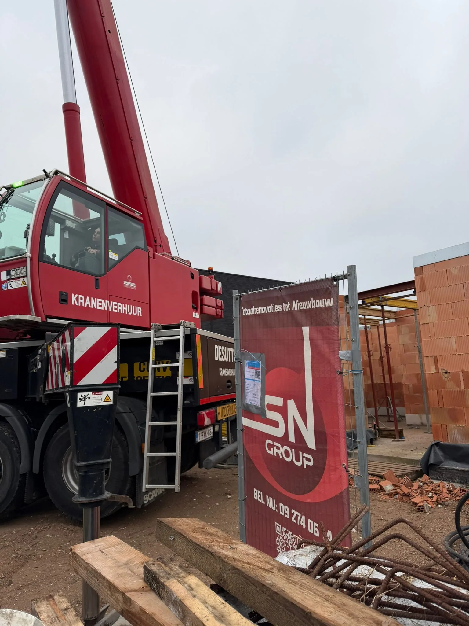 Kraan op een nieuwbouwwerf in Schelle, naast het werfbord van SN Group en de opgetrokken snelbouwmuren met stempels