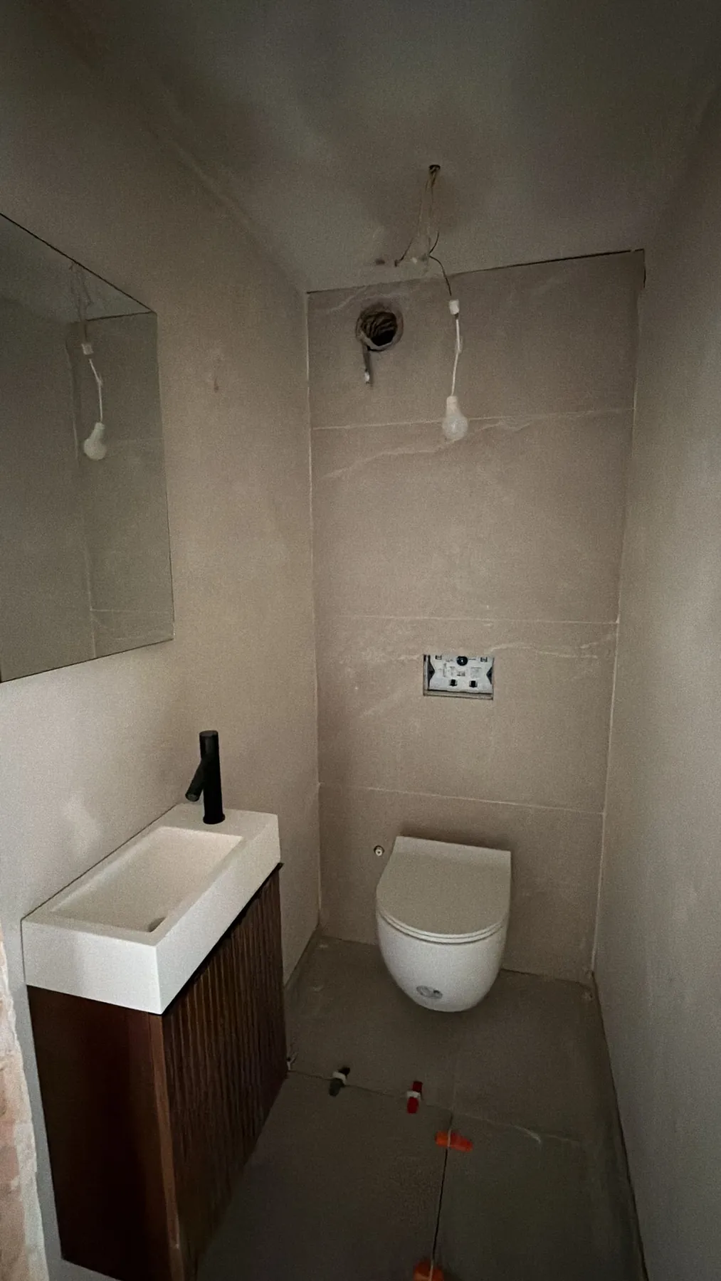 Apart toilet met een hangtoilet voor een betegelde wand en een wit fonteintje op een meubel in houtdecor