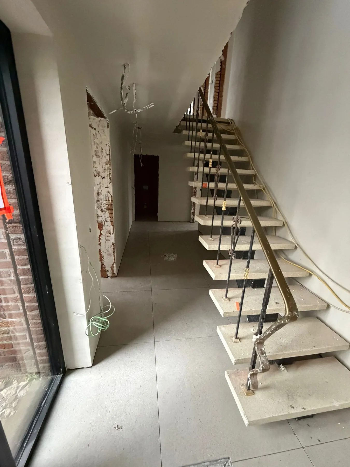 Dezelfde trap met lichte treden en dezelfde leuning, tussen witte gepleisterde muren, boven een betegelde vloer