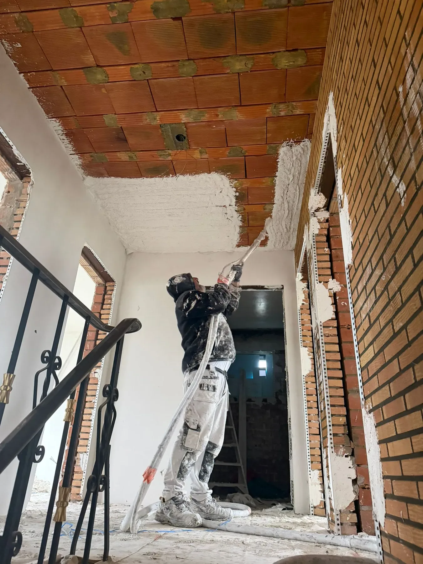 Stukadoor op de overloop zet pleister op het plafond van de traphal, dat nog uit rode bouwstenen bestaat
