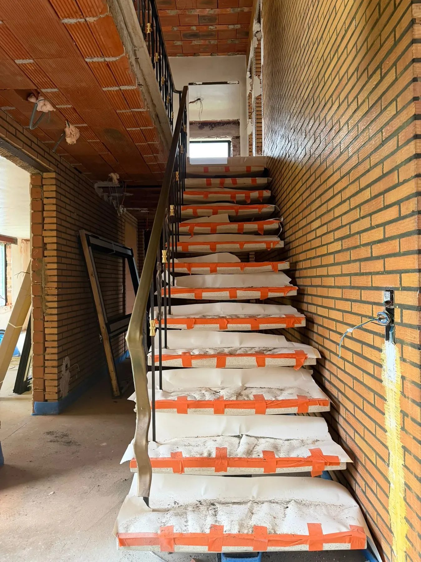 Trap met beschermde treden tussen bakstenen muren, onder een plafond van rode bouwstenen